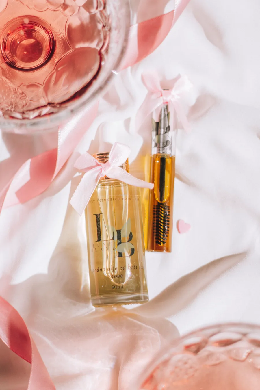 Botellas de perfume con listones rosas sobre una superficie clara